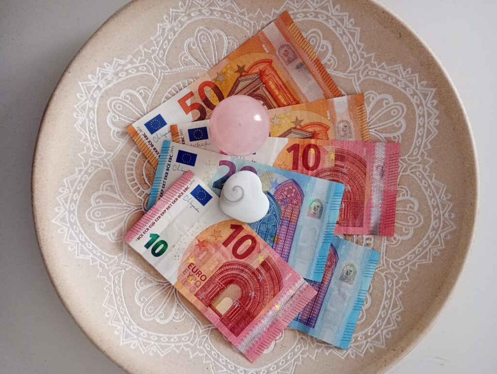 Dekorative Schale mit Mandala-Muster, gefüllt mit Geldscheinen und Kristallen – eine von vielen Methoden für das Öffnen des Nervensystems hin zum Empfangen und Fülle.